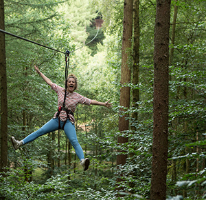 Image shows a girl making a star shape as she zooms down a zip line through the forest