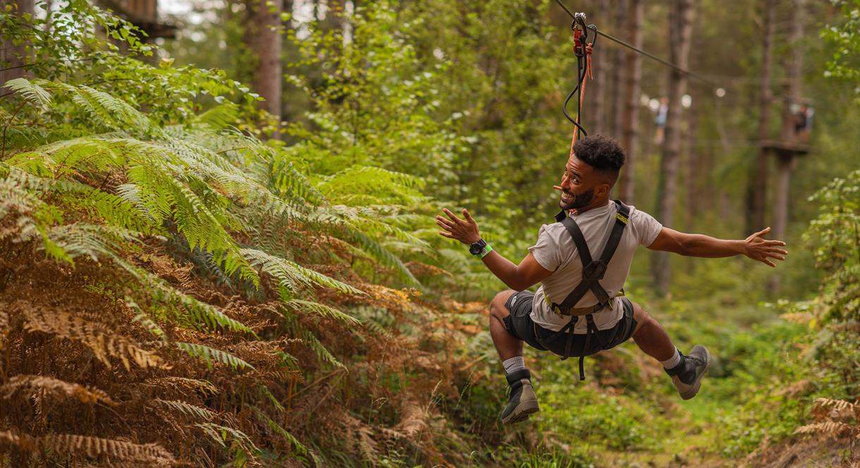 A man flies through the air, backwards, on a zip wire in a forest
