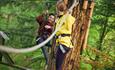 Two friends tackle the obstacles on a high ropes course in a forest