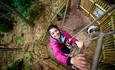 An intrepid visitor climbs a rope ladder and looks at the camera at a high ropes course
