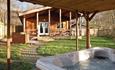 A hot tub on the porch of one lodge, looking over at another cabin, on a sunny day