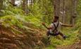 A man flies through the air, backwards, on a zip wire in a forest